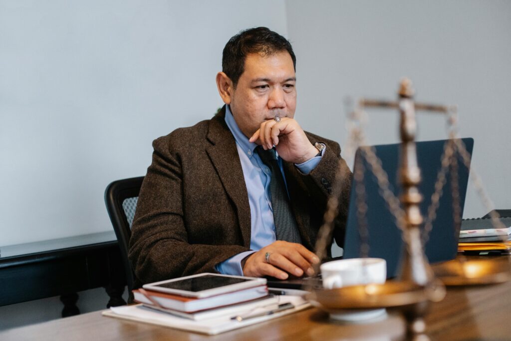 pexels photo 5668781 5668781 Serious adult Asian male judge in formal clothes browsing netbook and touching chin in thoughts while working in modern law office