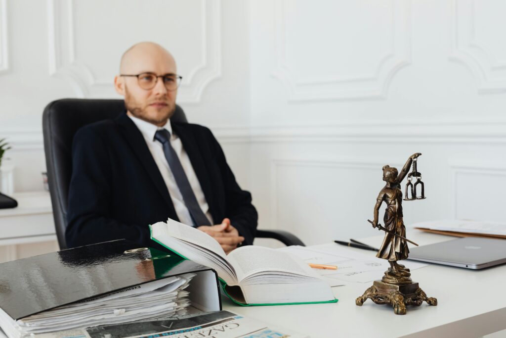 pexels photo 7876289 7876289 Bald lawyer in office sitting with legal documents and Justice statue.